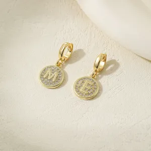 Close-up detail of gold-plated pavé cubic zirconia letter M and E pendant hoop earrings.