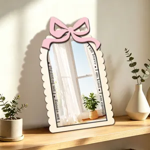 Close-up detail shot of wooden decorative mirror with pink bow and inspiring engraved text.