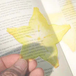 Close-up detail of the translucent star fruit acrylic bookmark resting on an open book page.