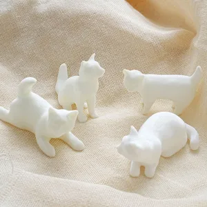Close-up detail of 3D printed white cat fridge magnets, cute animal figurines on textured fabric.