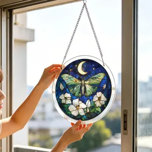 Detailed shot of circular acrylic moth suncatcher hanging in window with warm sunlight.