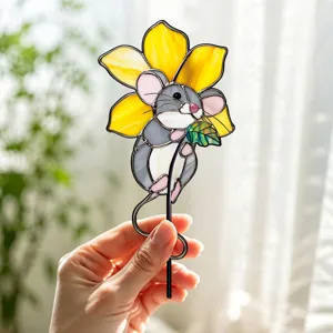 Détail d'un tuteur de jardin souris en verre coloré avec fleur jaune et feuille verte.