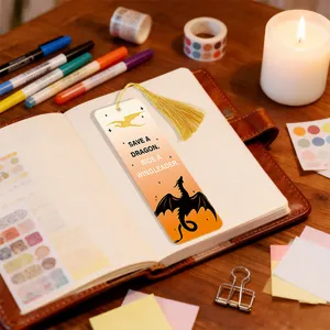 Close-up of decorative acrylic bookmark with golden tassel and dragon print on open notebook.