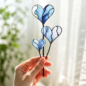 Vue détaillée de trois piques de jardin en cœur en verre teinté bleu tenues en main.