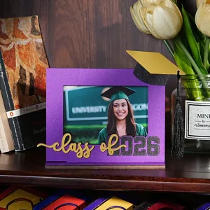 Dettaglio cornice per foto in legno con pannello viola, cappello dorato e scritta di laurea.