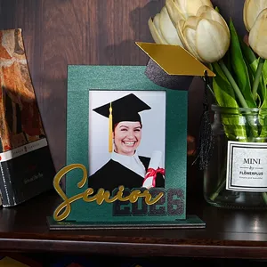 Dettaglio cornice portafoto in legno con decorazione laurea senior 2026 sul tavolo.