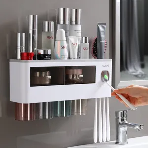 Wall-mounted toothbrush holder set with cups and automatic toothpaste dispenser for bathroom use.