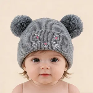 Joli bonnet en tricot gris avec broderie de chat et deux pompons pour bébé en détail.