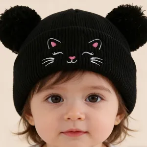 Gros plan d'un bonnet en tricot noir avec deux pompons et une jolie broderie de chat.