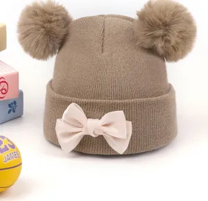 Vue détaillée d'un charmant bonnet bébé en tricot avec deux pompons et un nœud rose.