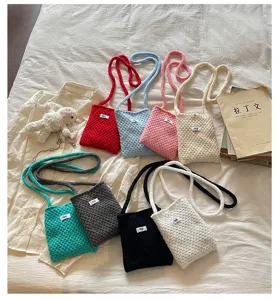 Détail de sac bandoulière en tricot coloré avec différentes teintes vives et petites étiquettes.