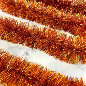 Orange tinsel garland detail close-up, thick shimmering party hanging decoration ribbon.