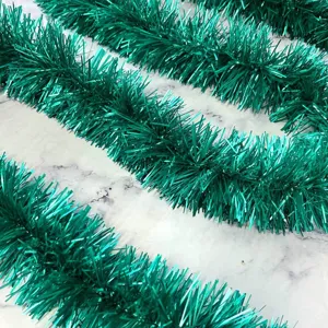 Green tinsel garland detail showing thick metallic fringe texture for holiday decoration.