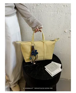 Detailed view of yellow suede dumpling bag with charms and zipper in minimalist style.