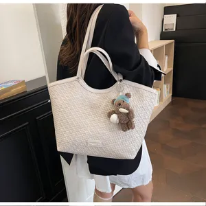 Close-up detail of stylish woven tote shoulder bag with cute plush bear keychain accessory.