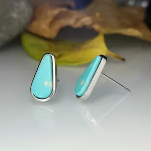 Gros plan détaillé de boucles d'oreilles clous en turquoise géométrique sur fond blanc.