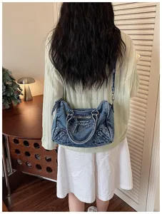 Detail view of retro washed denim motorcycle shoulder bag with metal zipper accents worn by model.