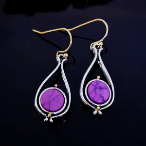 Detailed view of two-tone drop earrings featuring purple turquoise stones and golden hooks.
