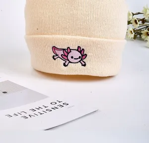 Close-up detail of beige knitted cuffed beanie with cute pink axolotl embroidery design.
