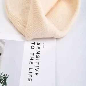 Close-up detail of a soft beige knitted beanie hat, showing fine texture and cozy fabric.