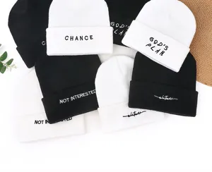 Detail view of stylish black and white knitted beanies with cool embroidered slogans for winter warm.