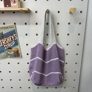 Gestrickte Häkel-Schulter-Tragetasche in Lila und Weiß, stilvoll an der Wand präsentiert.