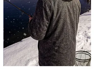 Detailaufnahme einer warmen Fleecejacke beim winterlichen Angeln in schneebedeckter Naturlandschaft.