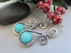 Gros plan de boucles d'oreilles artisanales en fil d'argent avec des perles de pierre bleue.