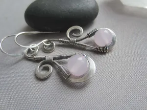 Gros plan détaillé de boucles d'oreilles en fil métallique avec de fines perles de quartz rose.