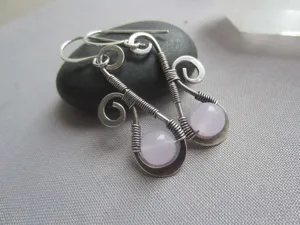 Gros plan détaillé de boucles d'oreilles artisanales en fil de fer avec perles de cristal rose.