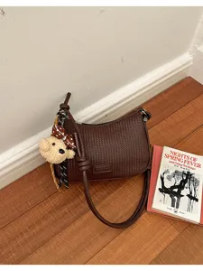 Detailed view of brown woven shoulder bag featuring soft leather and cute teddy bear charm.
