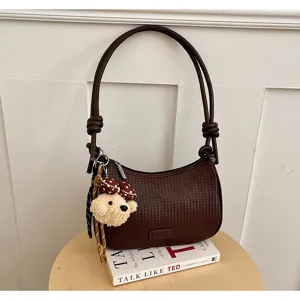 Brown woven shoulder bag detail featuring a cute plush bear keychain and elegant scarf charm.