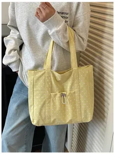 Vue détaillée d'un élégant sac cabas en toile à pois jaunes avec poche avant à cordon.