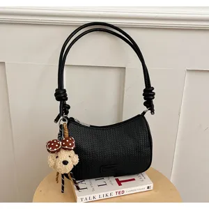 Detailed shot of stylish black woven shoulder bag with knotted straps and cute plush dog charm.