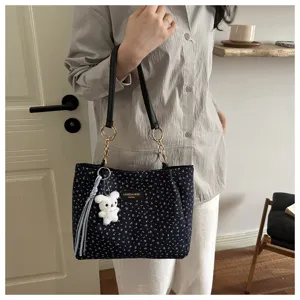 Blumen Schultertasche Detail mit elegantem Muster, Lederriemen und süßem Bärenanhänger.