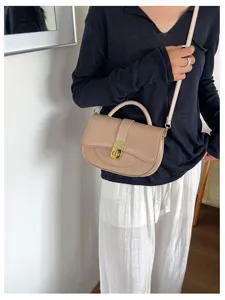 Primo piano di elegante borsa a sella beige con chiusura metallica e tracolla.