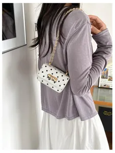 Stijlvolle schoudertas met wit-zwarte polkadotprint, gouden metalen ketting en slot.