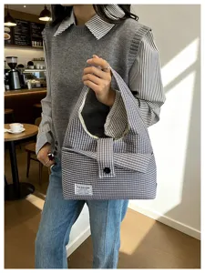 Detailed view of the gray plaid hobo shoulder bag worn by a model in a cozy cafe scene.