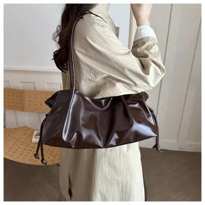 Detail shot of the glossy brown leather shoulder bag with side drawstrings worn by model.