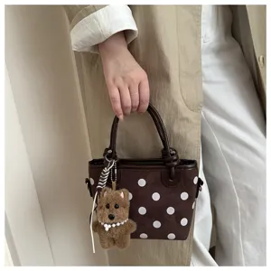Gros plan détaillé du sac à main marron à pois avec un joli pendentif ours en peluche.