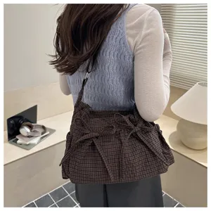 Vista dettagliata di un'elegante borsa a tracolla a quadri marrone con graziosi fiocchi.