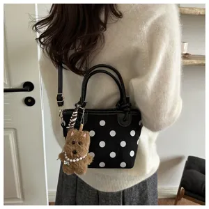 Close-up detail of black polka dot bucket bag with cute brown plush bear charm and shoulder strap.