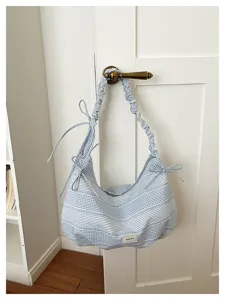 Detail view of blue and white striped canvas shoulder bag featuring chic bow and ruffle strap.