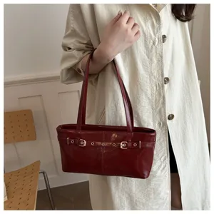 Detailed shot of a stylish burgundy patent leather shoulder bag with chic belt buckle decor.