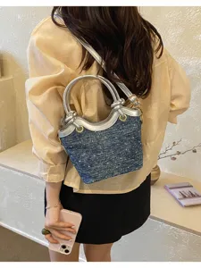 Trendy denim bucket bag detail, featuring metallic silver handles and adjustable shoulder strap.