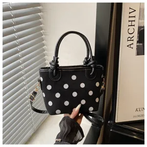 Sac seau noir élégant avec des pois blancs, poignées supérieures et bandoulière réglable.