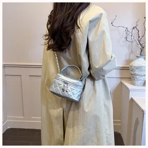 Détail de sac vanity matelassé argenté avec motif losanges, bandoulière chaîne et poignée.