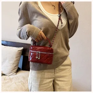 Gros plan du sac bandoulière matelassé rouge foncé avec chaîne et joli charm en forme de cœur.