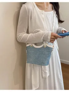 Detailed view of the stylish blue denim bucket handbag with white leather trim and metal rings.