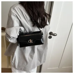 Vue détaillée d'un sac à bandoulière en cuir verni noir avec fermoir métallique.
